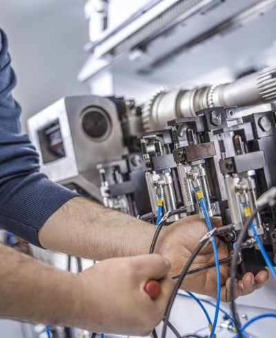Close up of service technician performing industrial machinery inspection and repair on electrical components